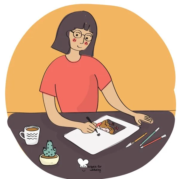 A person drawing at a table, with coloured pencils beside the page