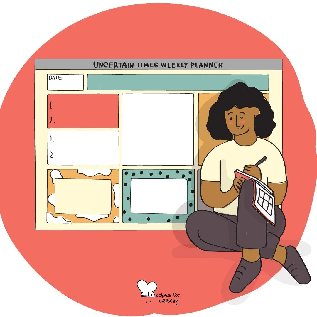 A person sitting on the floor writing in a notebook beside a large weekly planner